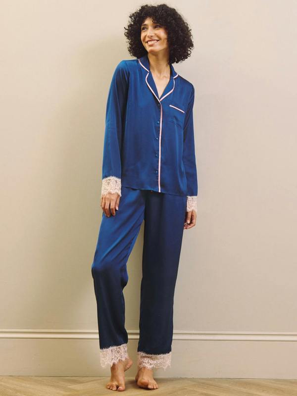 Woman wearing a blue satin pajama set with lace trim against a beige wall.