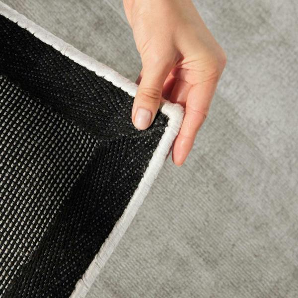 Person peeling back a gray rug to reveal black underlay