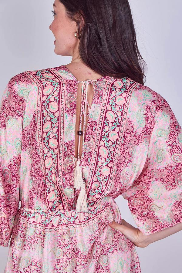 Woman wearing a pink and green patterned dress with tassels on a plain background