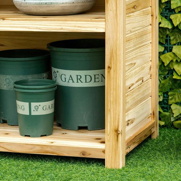 Lower shelf of natural wood potting bench holding green plant pots.