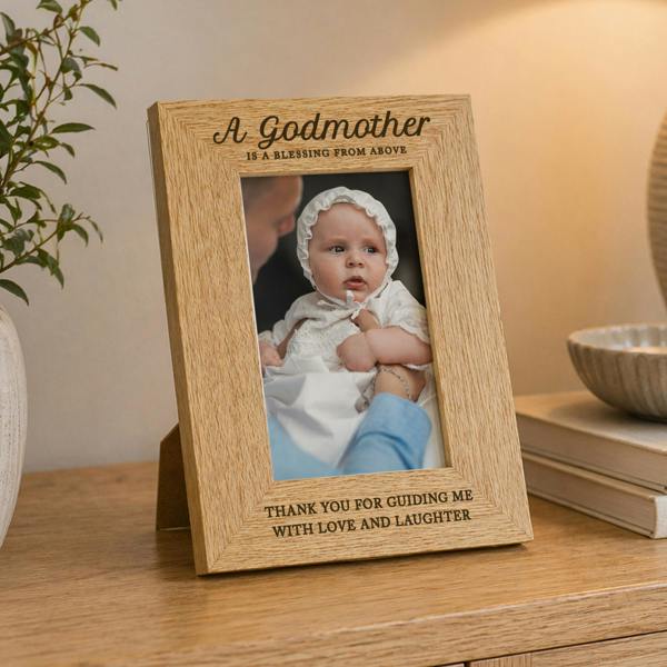 An engraved oak veneer picture frame holding a baby photo in a white christening bonnet, styled on a wooden tabletop with neutral decor.