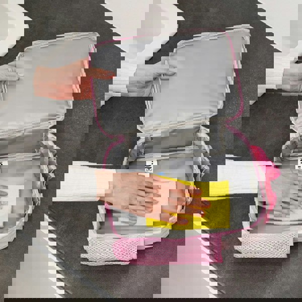 Hands cleaning pink insulated lunch bag with yellow cloth ON8 label visible on the interior in a kitchen setting with a dark countertop and white sink nearby