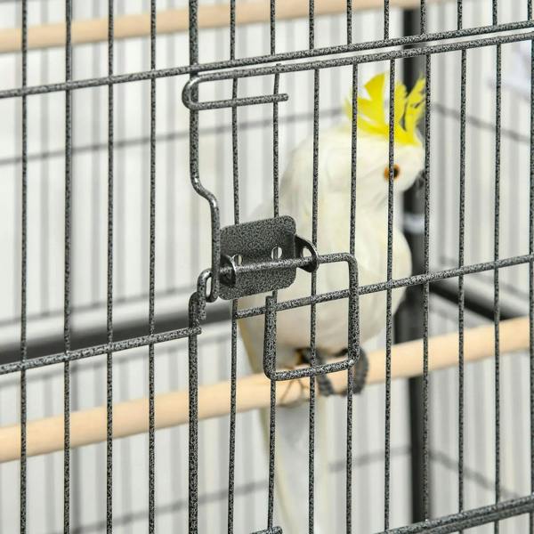 Close-up of dark grey bird cage door latch and wire bars with a small bird nearby