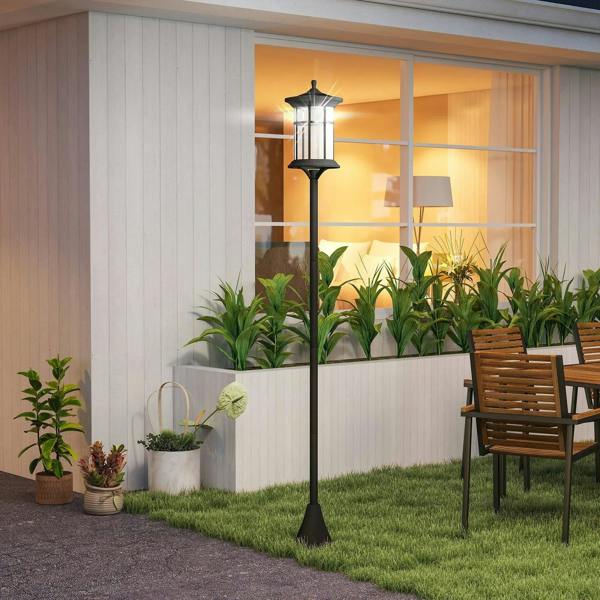 Black solar lamp post with glass lantern head in front of a house wall