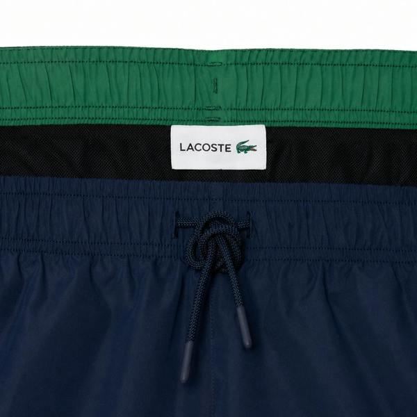 Lacoste navy blue swim shorts with green waistband, black mesh lining, and drawstring.