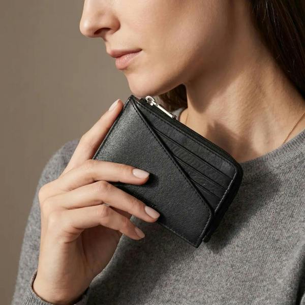 Woman holding a black wallet against a neutral background