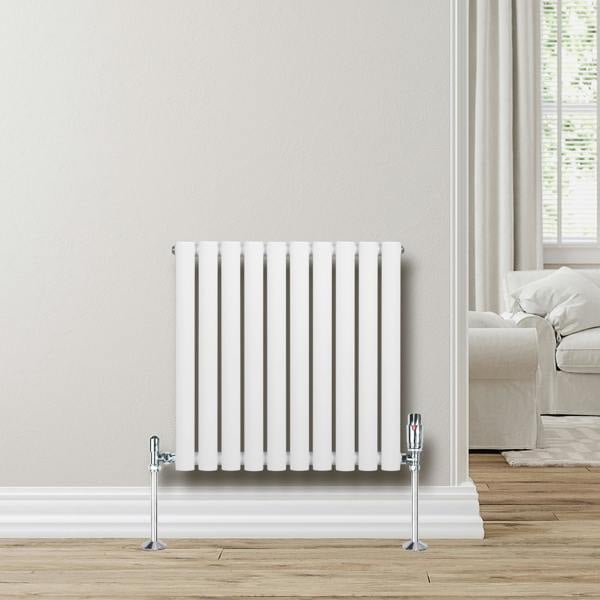 White oval single column radiator, 600 x 600mm, mounted on a light wall, with chrome valves and a wooden floor background