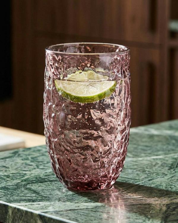 Two pink textured glasses on a wooden surface with a candle and greenery.
