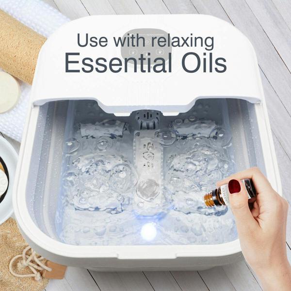 A person pours essential oil into the Rio Deluxe Foldaway Foot Spa Bath for a luxurious foot treatment; text above reads, Use with relaxing Essential Oils. Towels and soap can be seen nearby.