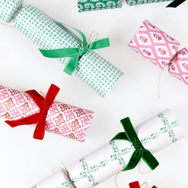 Close-up view of scalloped Christmas crackers showing block-print patterns, plush velvet ribbon bows, and metallic gold ties.