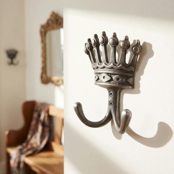 Close-up of vintage twin cast iron coat hook with royal crown, mounted on a painted wall in an entryway, highlighting detailed texture and design.