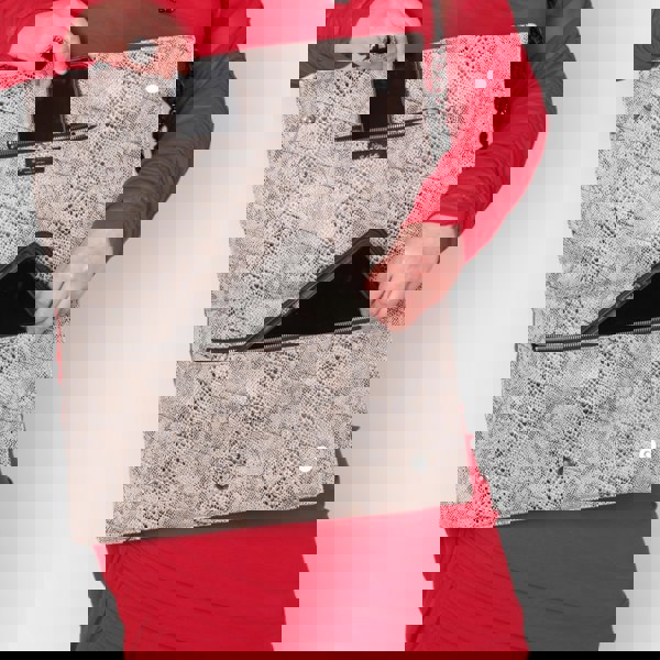 Person holding a snakeskin patterned laptop clutch bag with aluminium chain strap showing a phone inside and an Ipad , wearing a red outfit.