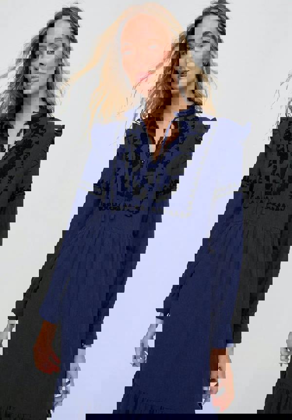 Woman wearing a navy blue dress with intricate black embroidery on a white background