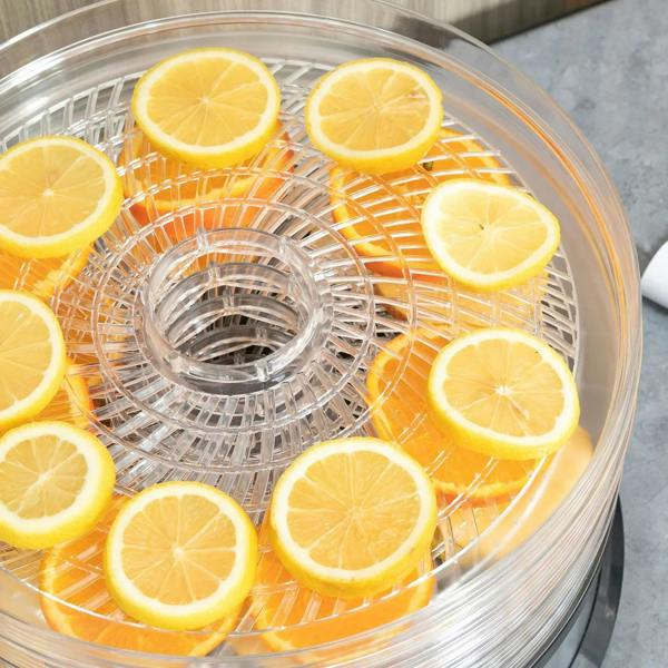 Lemon slices arranged on the wire tray inside a clear 5-tray dehydrator lid