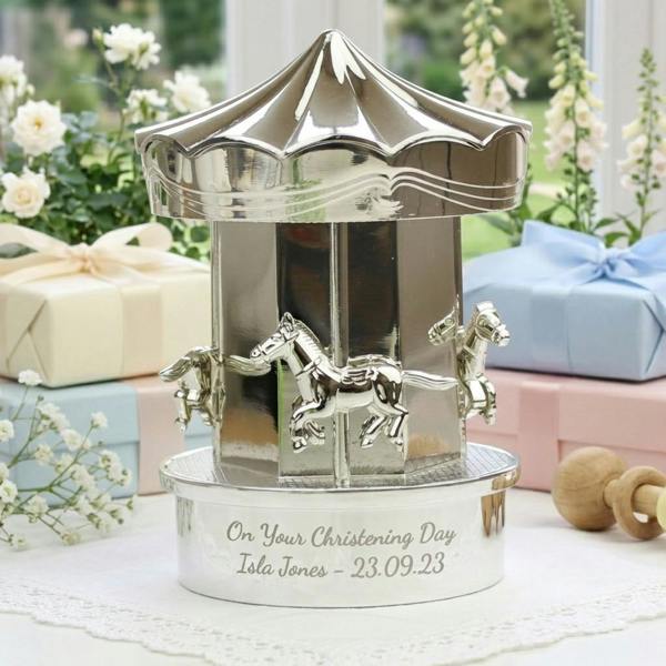 A personalised silver-plated carousel money box engraved with a Christening message, displayed on a lace table runner alongside wrapped gift boxes.