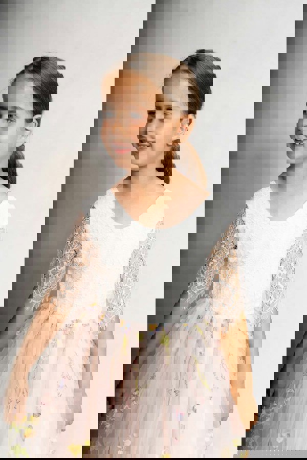 Young girl wearing a white dress with floral details on a plain background