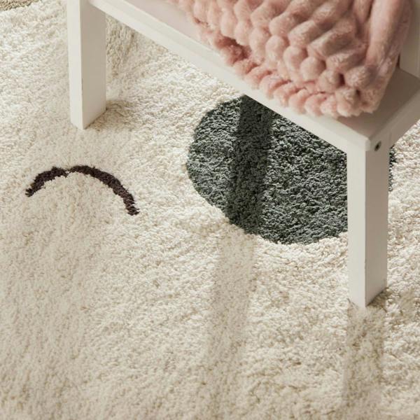 Close-up of a white rug with a chair and pink blanket on a light-colored floor.