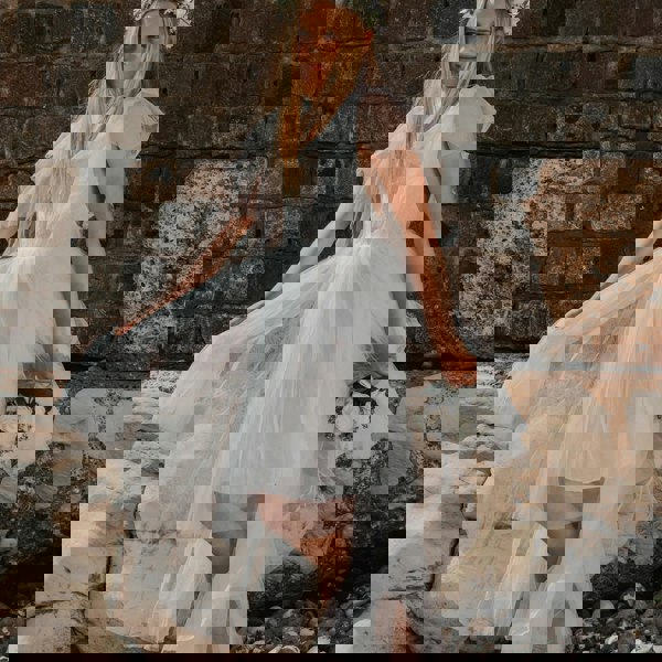 girl in a white dress standing against a stone wall.