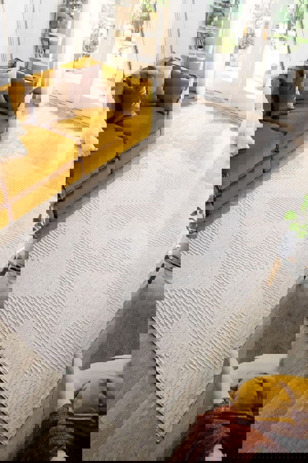 Abstract geometric rug in cream tones, enhancing a modern living room with yellow couch and natural light.