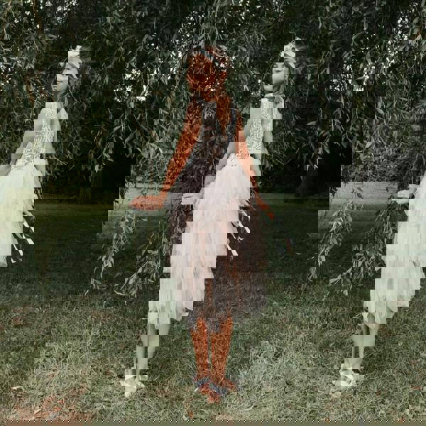 Young girl in a white dress standing in a natural setting with trees and grass.