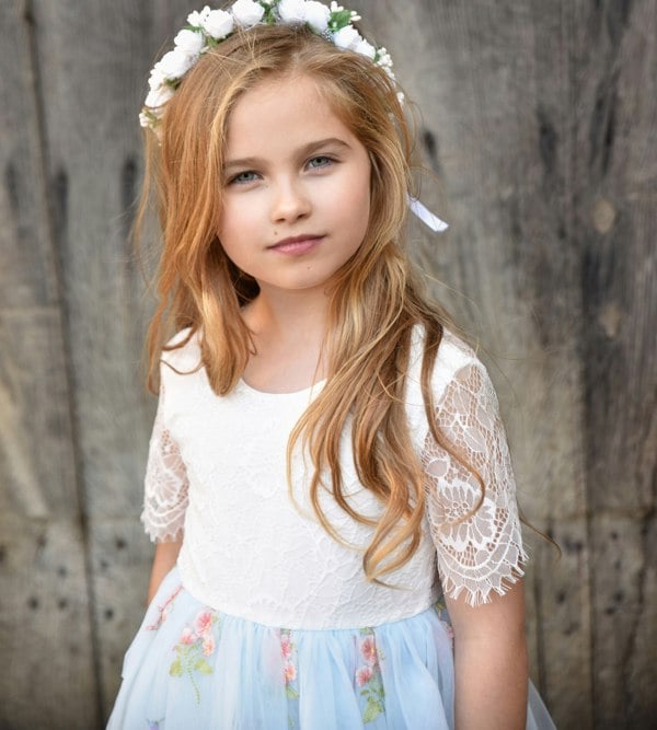 Young girl wearing a white lace top and floral skirt with a wooden background
