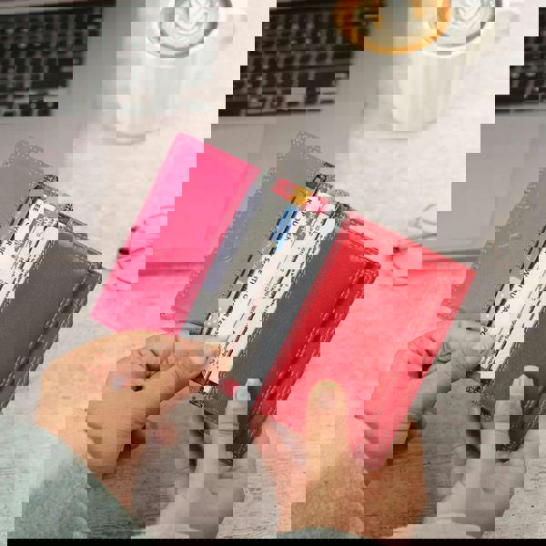 Person holding a pink wallet with cards, laptop, and coffee cup in the background