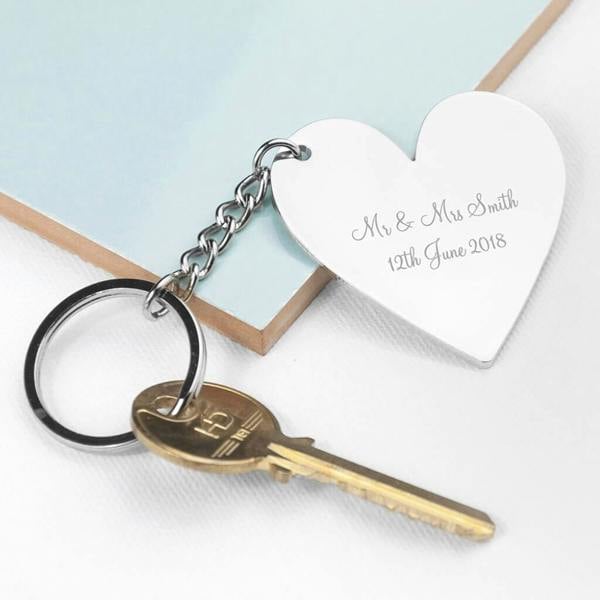 A silver-plated heart-shaped keyring resting on a table, engraved with "Mr & Mrs Smith 12th June 2018", attached to a single key.