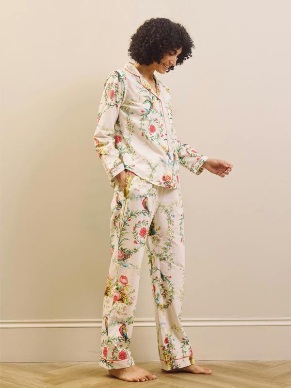Woman wearing floral pajamas standing against a plain wall.