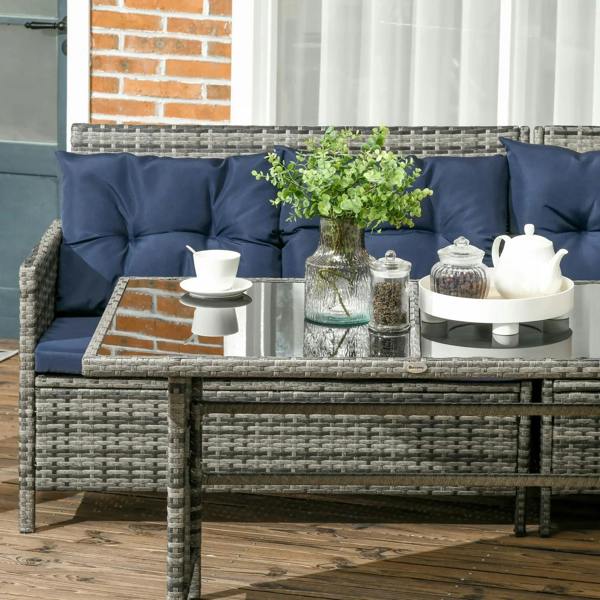 Lounge-style rattan patio sofa with dark blue cushions and glass coffee table