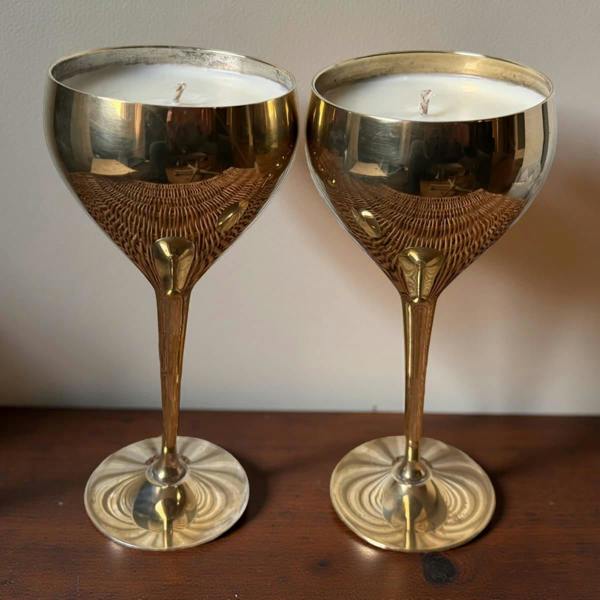 Two brass candle holders with wicker bases on a wooden surface.