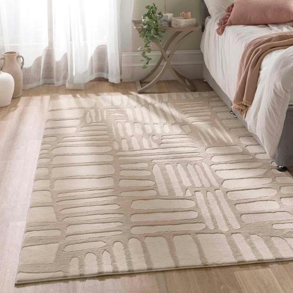 Beige patterned rug on a wooden floor in a bedroom setting.