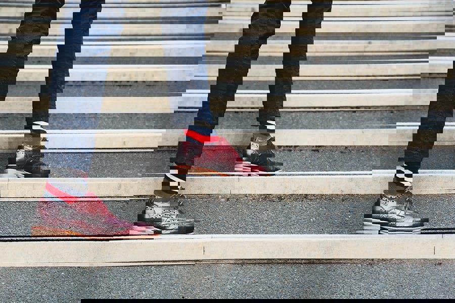 Person wearing maroon shoes and colourful stripe socks walking up a set of stairs.