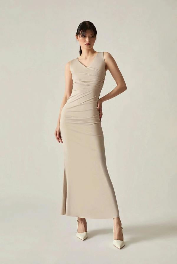 Woman in a beige dress standing against a soft beige background.