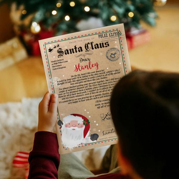 A child in a maroon jumper holding an official vintage parchment letter from Santa Claus personalised for Stanley.