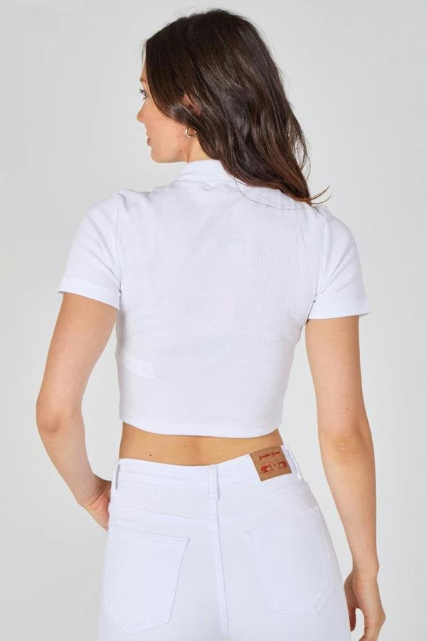 Woman wearing a white polo shirt and white pants against a plain background