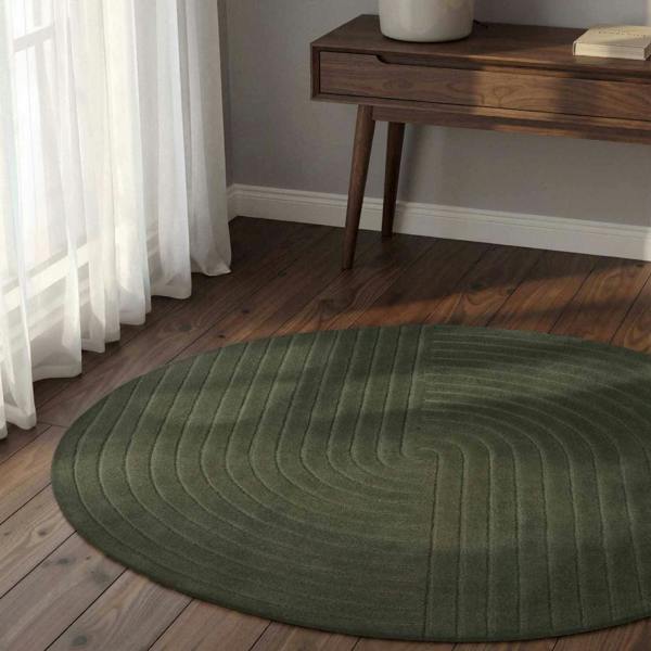Green round rug on a wooden floor with a wooden side table and white curtains.