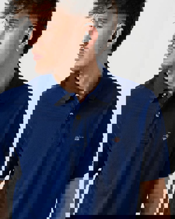 Model wearing GANT Mens Regular Fit Short Sleeve Shield Logo Pique Polo in 432 Rich Navy - Detail