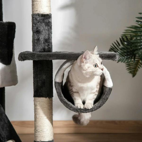White cat resting in a dark plush hanging hammock on an indoor cat tree