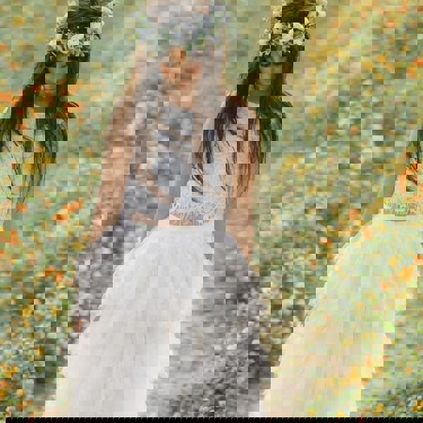 Woman in a white dress with a floral crown standing in a field of flowers.