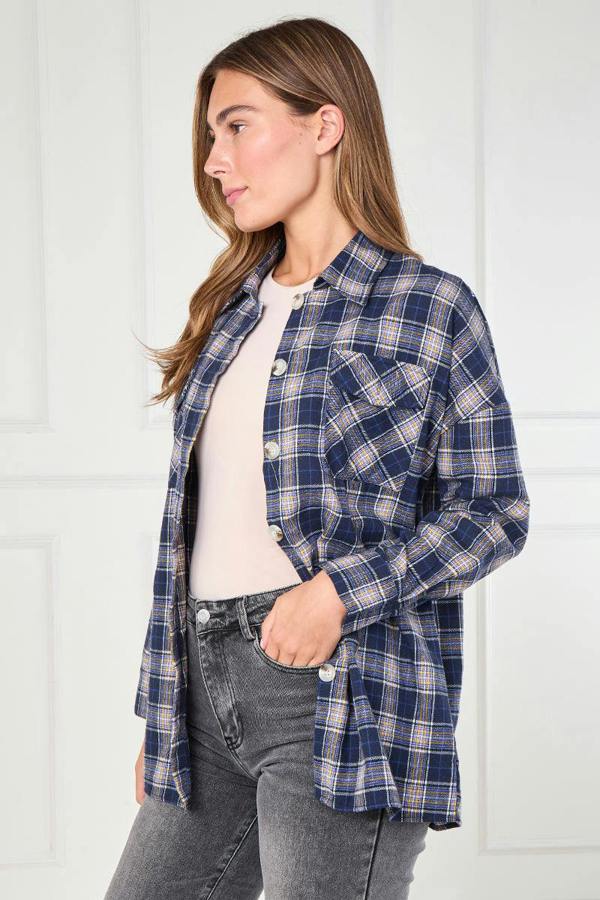 Woman wearing a blue plaid shirt over a white top with gray jeans against a white background