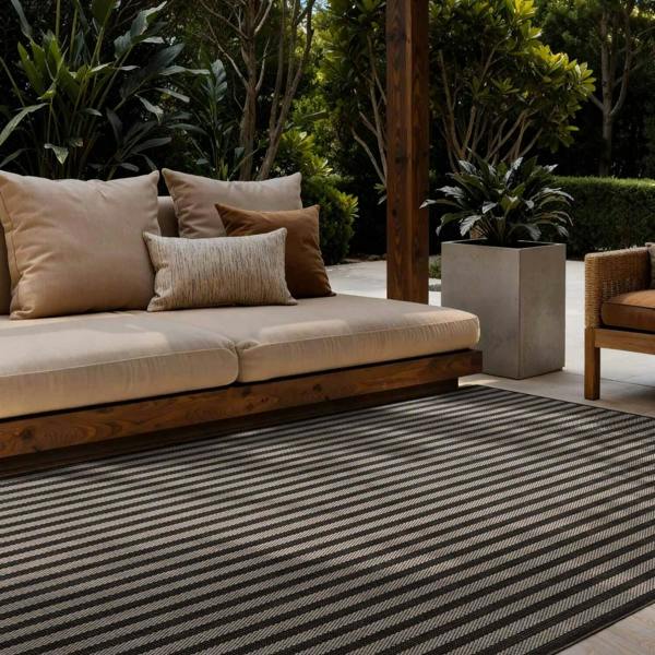 Outdoor seating area with a striped rug, cushions, and plants.