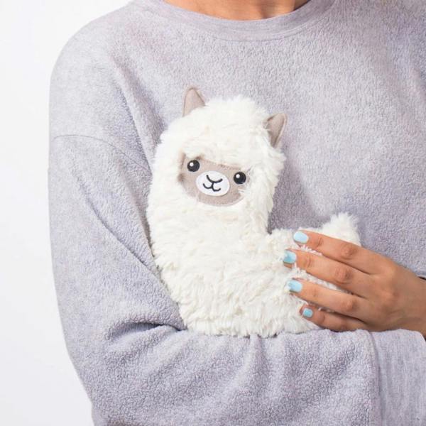 A woman holding a white, fluffy, microwaveable llama-shaped lap warmer.