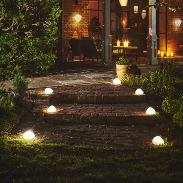 Multiple frosted glass solar pebble lights lighting up brick patio steps at night next to an illuminated house.