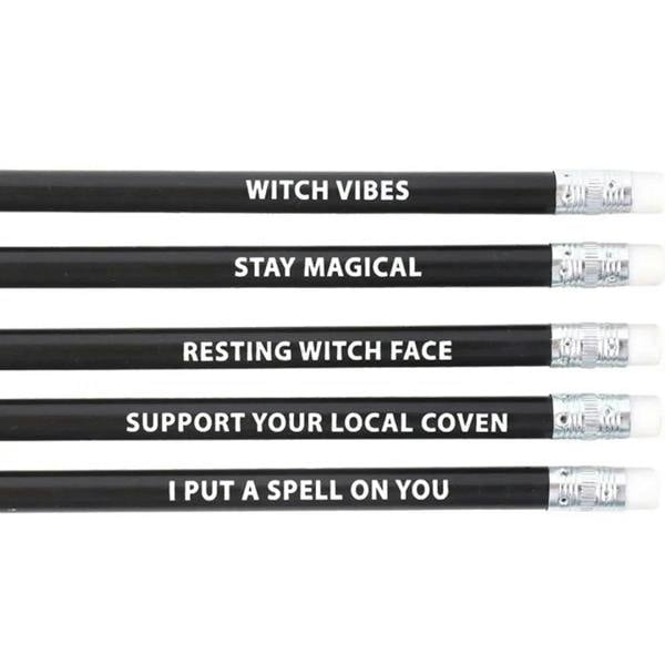 Close-up of black witch-themed pencils with white slogan text and silver erasers