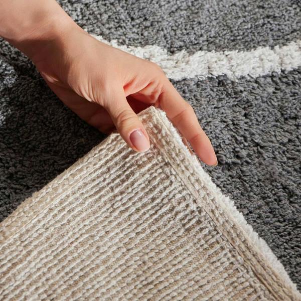 Hand holding a beige textured rug against a gray and white striped background