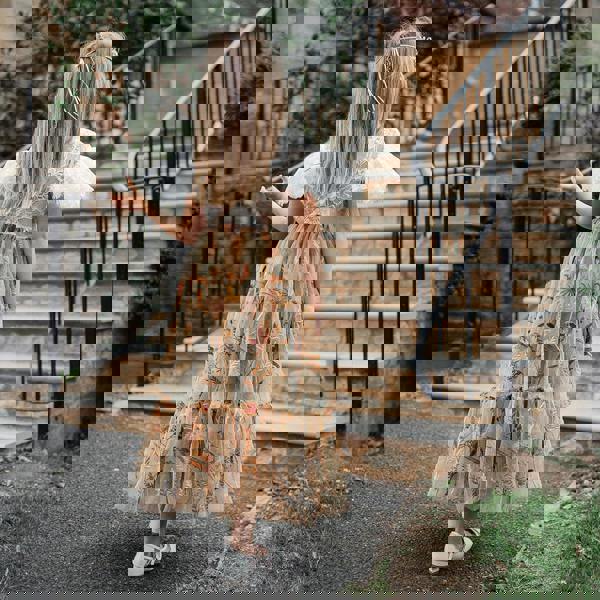 Child in a floral dress walking away from a stone building with steps.