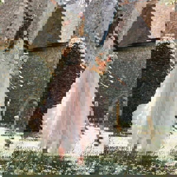 GIRL in a white lace top and blush skirt standing in a garden with a church in the background