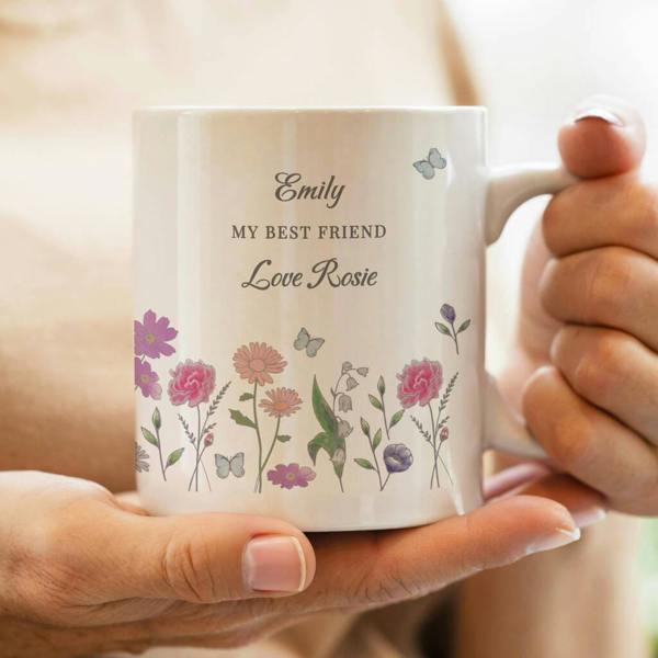 A person holding a personalised white ceramic mug printed with colourful wildflowers, butterflies, and the words Emily MY BEST FRIEND Love Rosie.