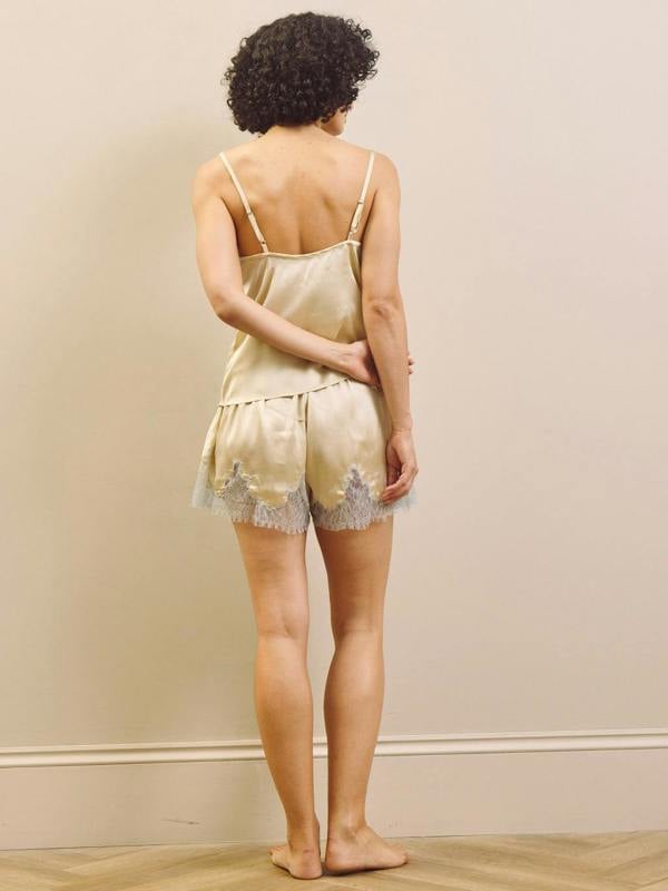 Woman wearing a light-colored satin nightgwear with lace trim against a plain wall.