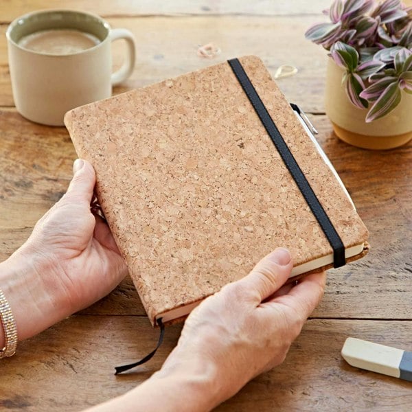 A person holding a cork notebook on a wooden table.